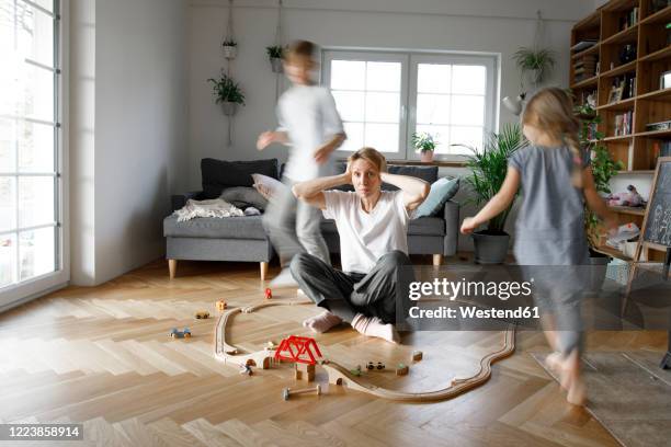 stressed out mother sitting in the middle of toys, while children are running around her - woman home run stock pictures, royalty-free photos & images