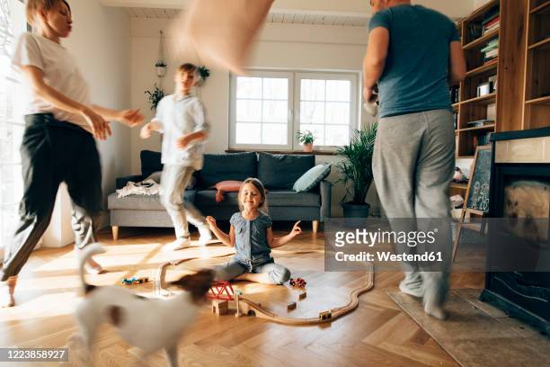 little girl meditating in the middle of toys, while family are running around her - mother running stockfoto's en -beelden
