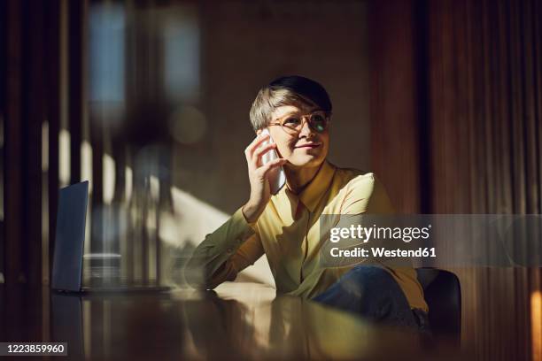 businesswoman sitting in her sustainable office, talking on the phone - vie simple photos et images de collection