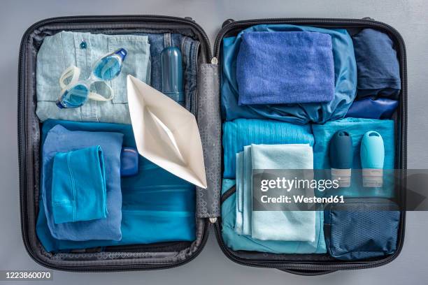 overhead view of packed suitcase with clothes, swimming goggles and paper boat - open suitcase stockfoto's en -beelden