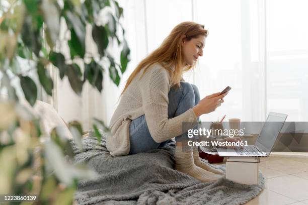 young woman using smartphone and laptop at home - woman using smartphone with laptop stock-fotos und bilder