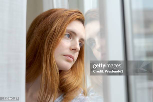 portrait of serious young woman looking out of window - pessimism stock pictures, royalty-free photos & images