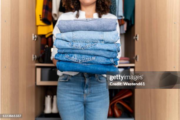 woman standing on front of wardrobe holding stack of blue jeans - kleiderschrank frau stock-fotos und bilder