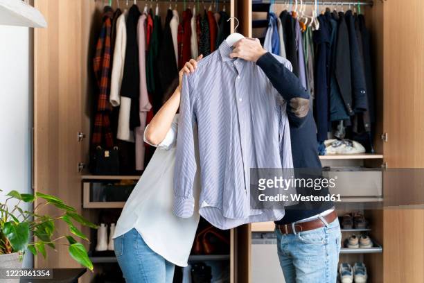 copule clearing out her wardrobe hiding behind a shirt - kleiderschrank frau stock-fotos und bilder