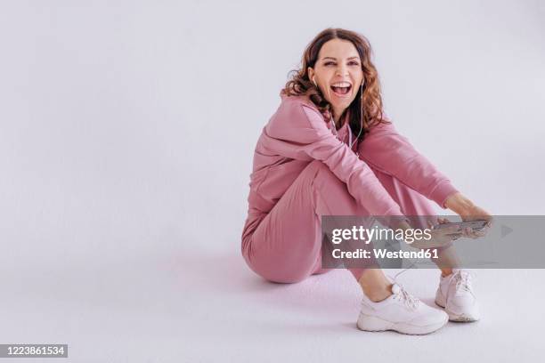brunette woman wearing pink track suit and listening to music, holding smartphone - pink sneakers fotografías e imágenes de stock