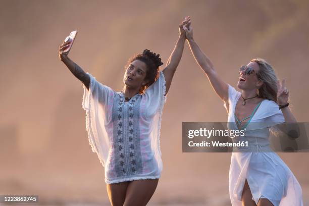 two happy women taking selfie on the beach, costa rica - tuniek stockfoto's en -beelden