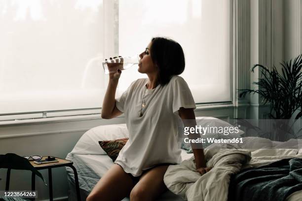 mature woman sitting on bed in the morning drinking water - drink photos et images de collection
