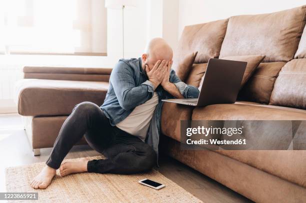 tired businessman with laptop covering face while sitting in living room at home - fatigue full body stock-fotos und bilder