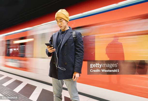 stylish man with smartphone and earphones in metro station - lange sluitertijd stockfoto's en -beelden