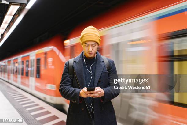 stylish man with smartphone and earphones in metro station - metrostation stockfoto's en -beelden