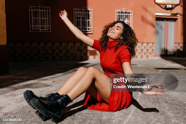 young woman wearing red dress and sitting on ground - stiefel stock-fotos und bilder