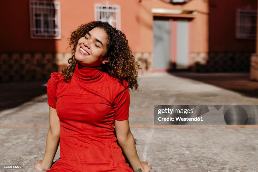 Smiling young woman wearing red dress and sitting on ground