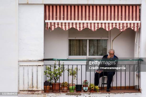 80 years old man talking on the phone on the terrace during the confinement by the covid-19 - state of emergency stock pictures, royalty-free photos & images