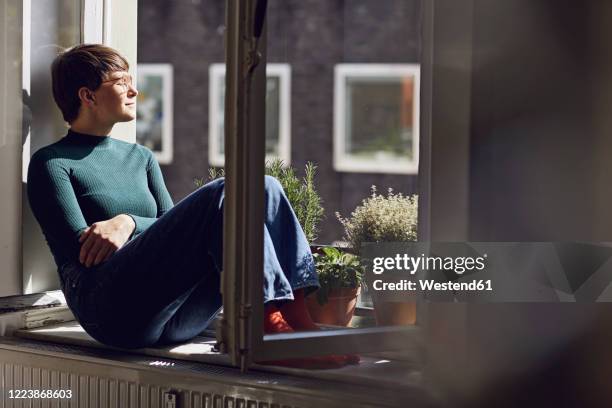 woman sitting at the window at home - window sill stock pictures, royalty-free photos & images