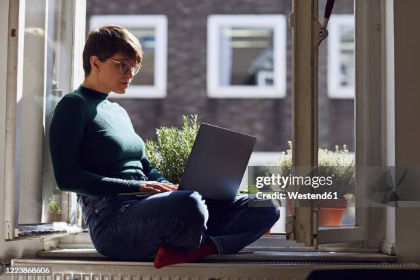 woman sitting at the window at home using laptop - windowsill copy space stock pictures, royalty-free photos & images