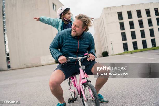 playful father with daughter on her bicycle - misbehaving children stock pictures, royalty-free photos & images
