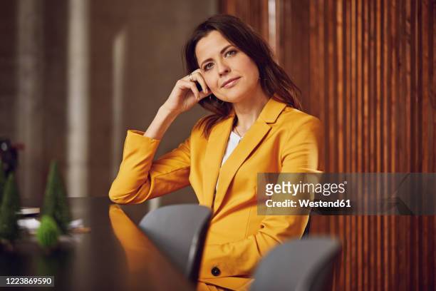 portrait of businesswoman wearing yellow suit sitting at desk in office - blazer jaune photos et images de collection