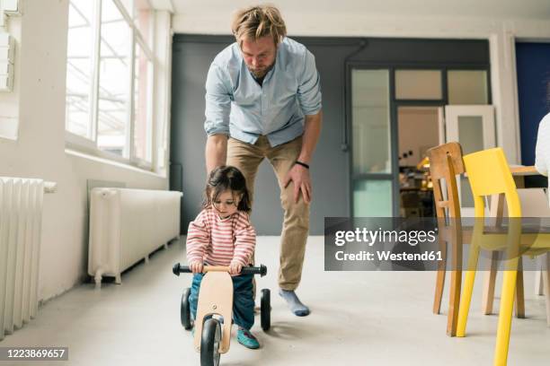 father watching daughter using balance bicycle - bicycle daughter stock-fotos und bilder