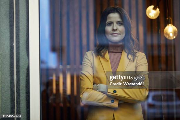 portrait of confident businesswoman wearing yellow suit standing behind windowpane - yellow blazer ストックフォトと画像