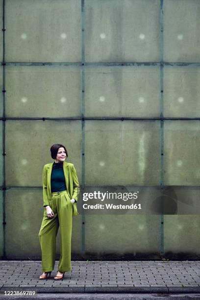 elegant businesswoman wearing green suit standing at a wall - traje verde fotografías e imágenes de stock