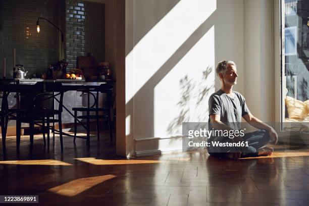 mature man sitting on the floor at home meditating - meditieren stock-fotos und bilder