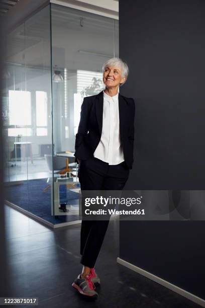 portrait of fashionable senior businesswoman wearing pantsuit and sneakers in office - smart fashion stock-fotos und bilder