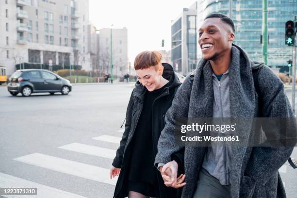 happy young couple crossing a street in the city, milan, italy - crossing stock pictures, royalty-free photos & images