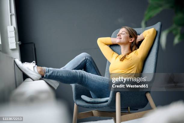 smiling young woman relaxing in armchair - feet up stock pictures, royalty-free photos & images