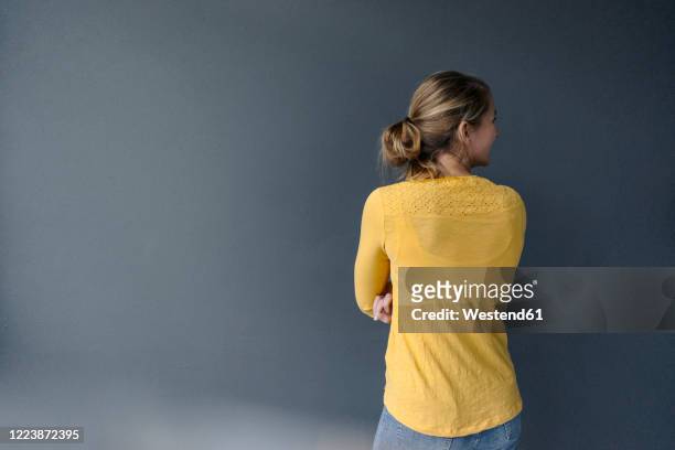 rear view of young woman standing at a grey wall - vista posteriore foto e immagini stock