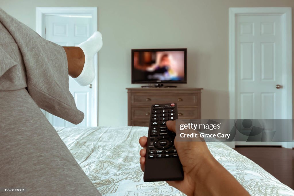 Woman Lounges in Bed Watching TV