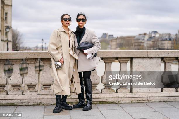 Guest wears earrings, sunglasses, a chain necklace, a metallic-tone chainmail bag, a beige jacket, beige pants, a beige flowing trench coat, black...