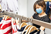 Asian woman shopping apparels in clothing boutique with protective face mask as new normal requirement