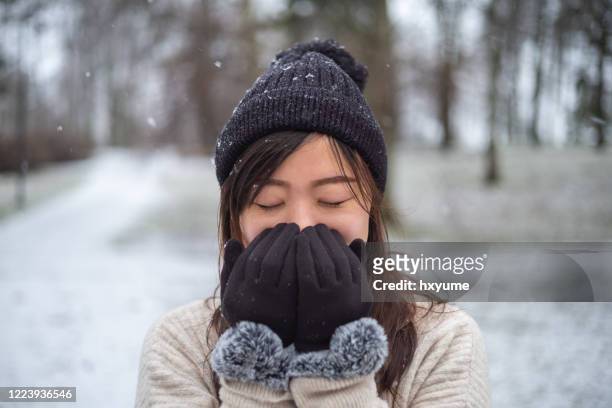 jonge aziatische vrouw warmt op en verwarmt handen dichtbij mond in de winterpark - warme kleding stockfoto's en -beelden