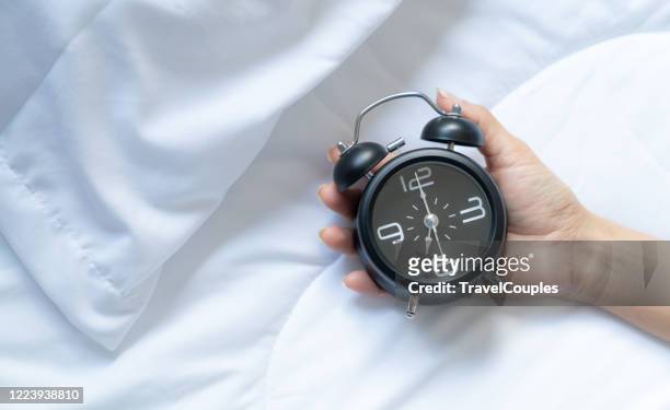 sleepy young woman stretching hand to ringing alarm to turn it off. early wake up. sleepy woman reaching holding the alarm clock in the morning with late wake up. every day life at home concept - alarm clock stock-fotos und bilder