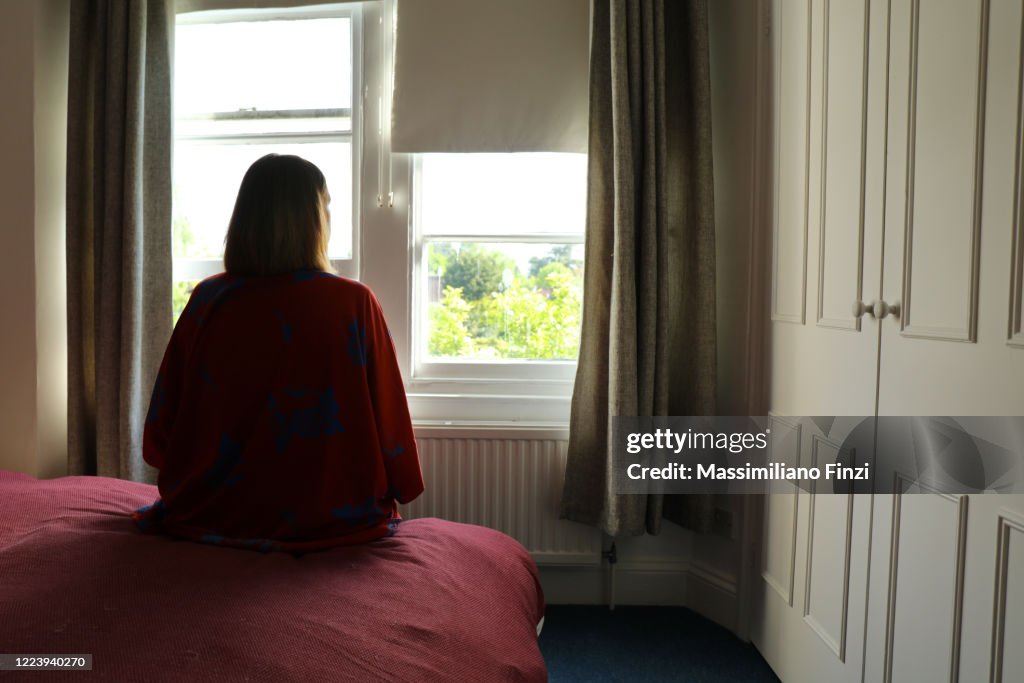 Lone woman sitting on the bed looking out of the window.