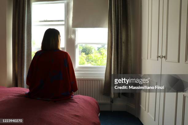 lone woman sitting on the bed looking out of the window. - loneliness stock pictures, royalty-free photos & images