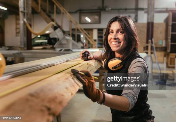 donna sorridente e misura tavola di legno in un woorkshop di falegnameria - carpenteria foto e immagini stock