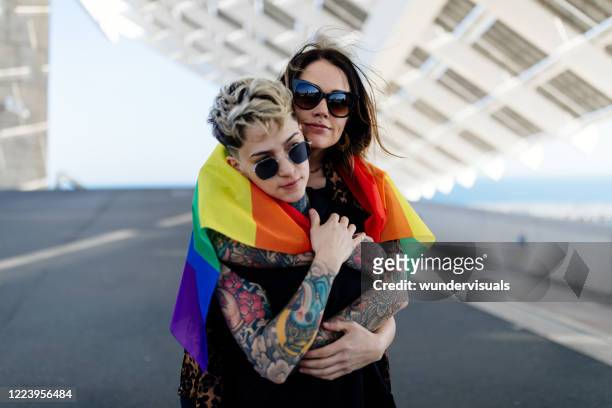 pareja lesbiana abrazándose entre sí con bandera arco iris orgullo lgbt - personas lgtbqi fotografías e imágenes de stock
