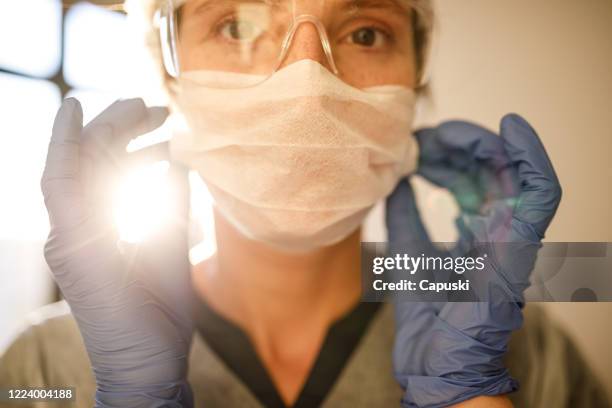 female health care worker putting mask on - infectious disease prevention stock pictures, royalty-free photos & images