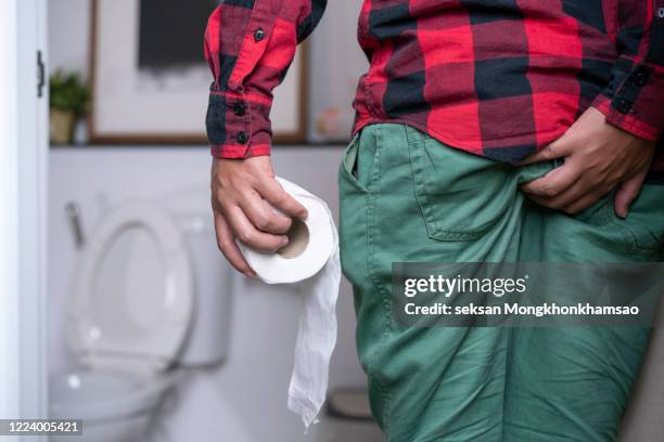 man holding toilet paper roll in bathroom - emorroidi foto e immagini stock