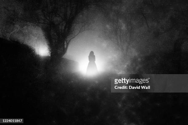 a country lane, on a foggy night with a ghostly woman in a dress. in front of glowing lights. with a grunge, blurred, vintage edit - spooky road stock pictures, royalty-free photos & images