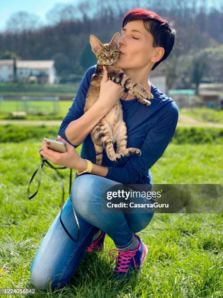 erwachsene besitzerin hugging und küssen devon rex katze im lokalen öffentlichen park am sonnigen nachmittag - stock photo - weidekätzchen stock-fotos und bilder