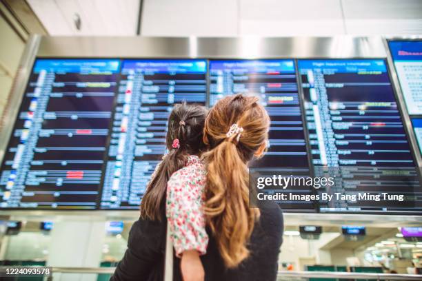 back view of mom & daughter checking flight status board at airport - holiday arrival stock pictures, royalty-free photos & images