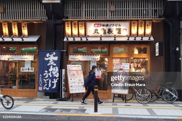 Woman wearing a face mask walks past an udon restaurant amid the coronavirus pandemic on May 9, 2020 in Tokyo, Japan.