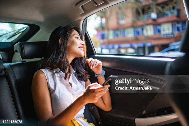 giovane vacanziere femminile con smartphone nel backseat del taxi - passeggero foto e immagini stock