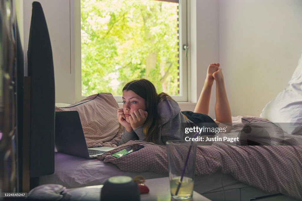 Bored teenage girl using laptop on her bed