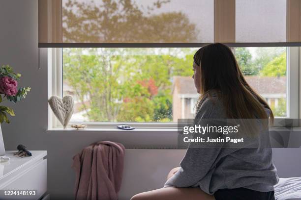 teenage girl looking out of bedroom window - solitario foto e immagini stock