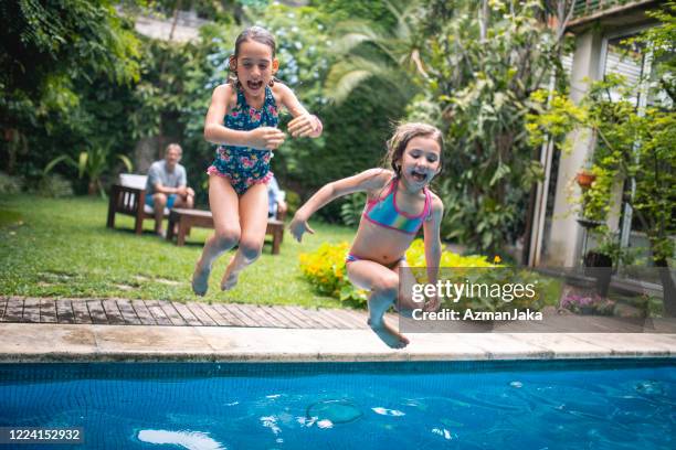 young girls jumping into family swimming pool - cannon ball pool stock pictures, royalty-free photos & images