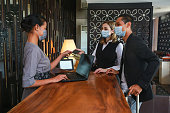 Couple and receptionist at counter in hotel wearing medical masks as precaution against virus. Couple on a business trip doing check-in at the hotel
