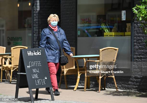 Lady wearing a face mask walks past an empty cafe on the first day restaurants and cafes have been allowed to reopen since March in the state of...